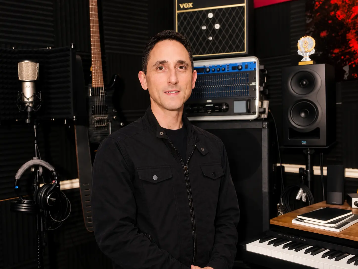 Theron Rodriguez, founder of Whole Earth Gifts, in his home studio with a microphone, guitar and mixing console.